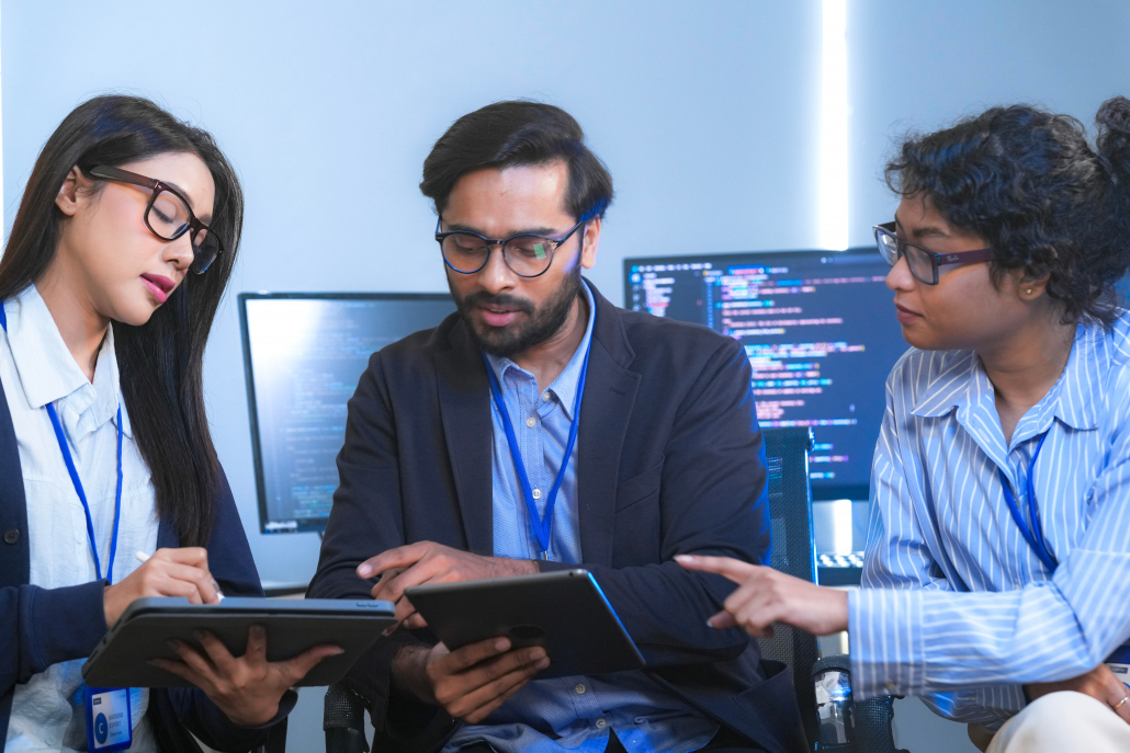 Diverse team of software engineers and data scientists collaborating on a project, using tablets and analyzing code. Concept for AI development, cybersecurity, and tech innovation.